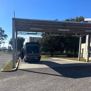 Exterior view of a covered drop-off area with a parked van and nearby people.