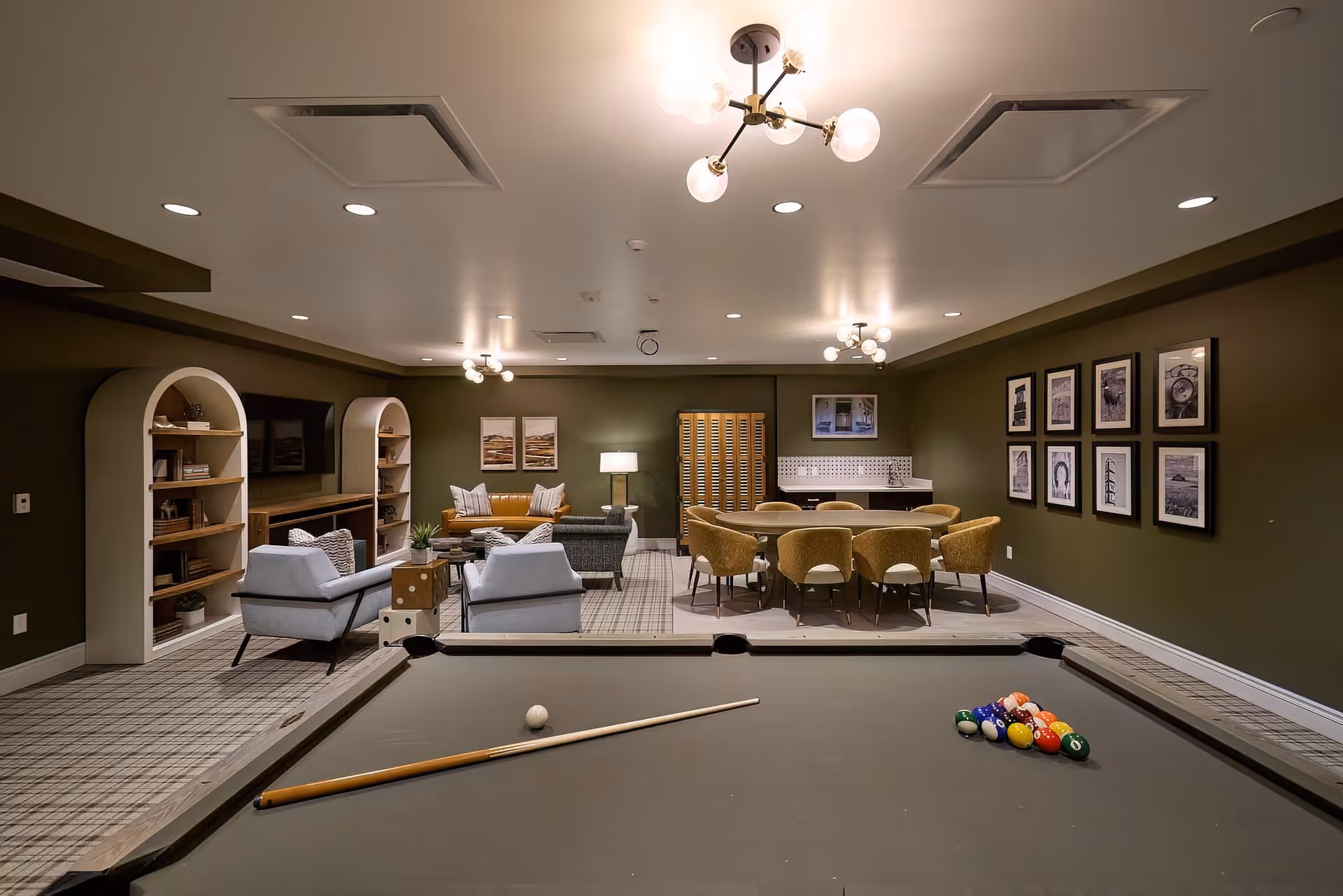A stylish communal lounge featuring a pool table in the foreground with seating and a dining area in the background.