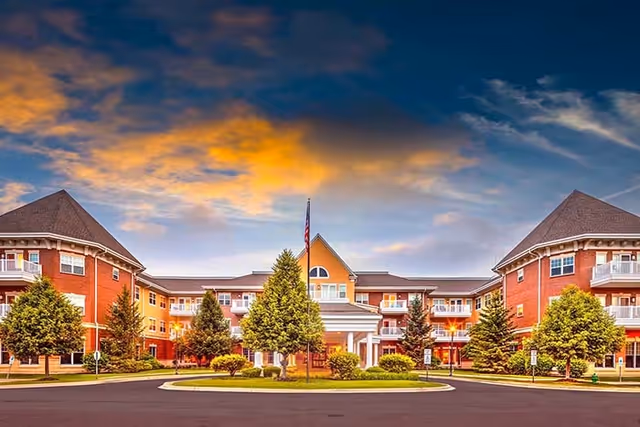 Front exterior view of The Holmstad, a senior living facility, with a circular driveway and trees.