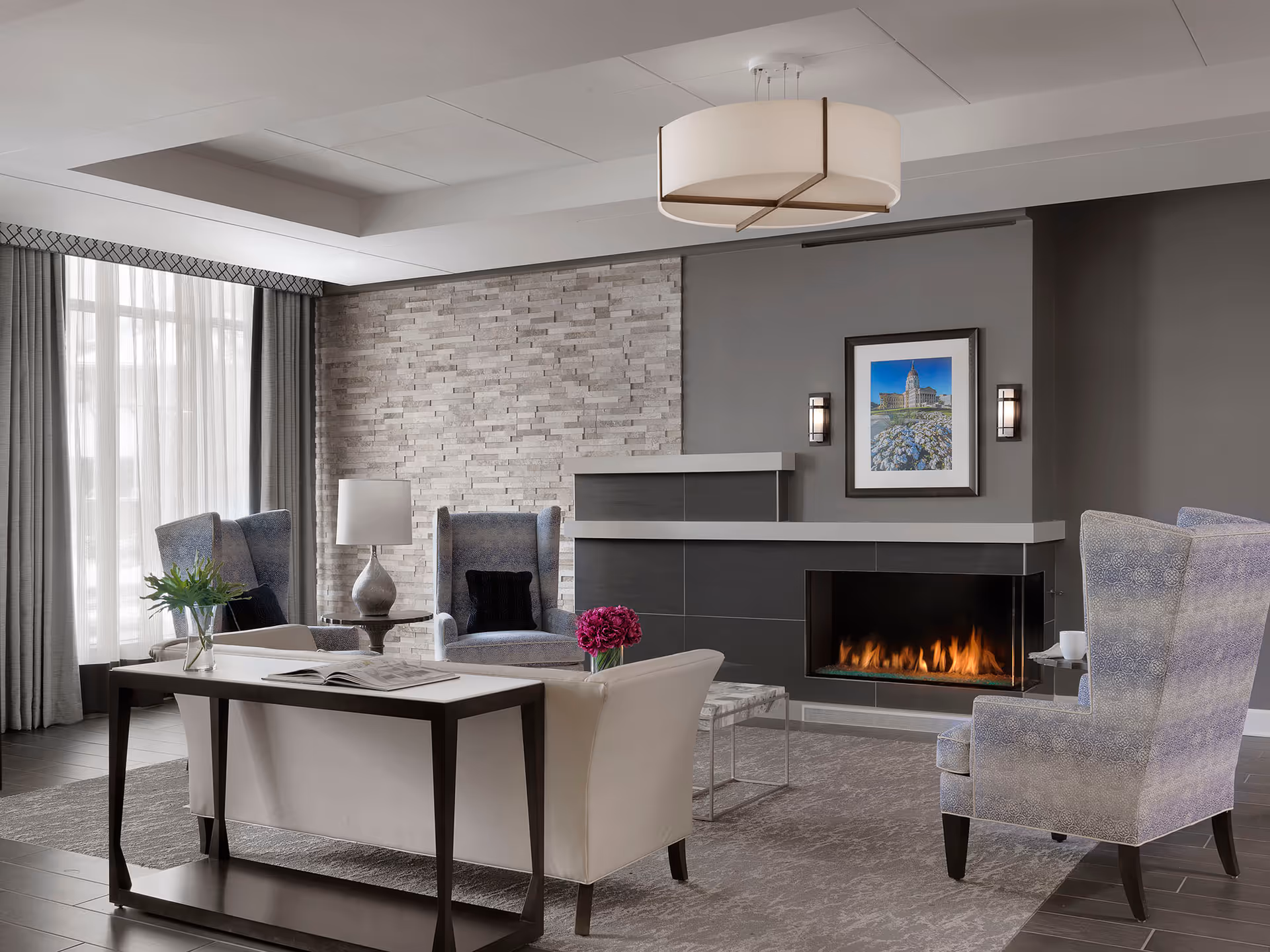 Contemporary living room with a fireplace, armchairs, sofa, side table with flowers, and framed artwork.