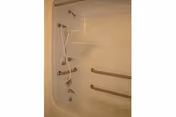 Bathtub/shower unit with a handheld showerhead, built-in shelves, and two horizontal grab bars for accessibility.