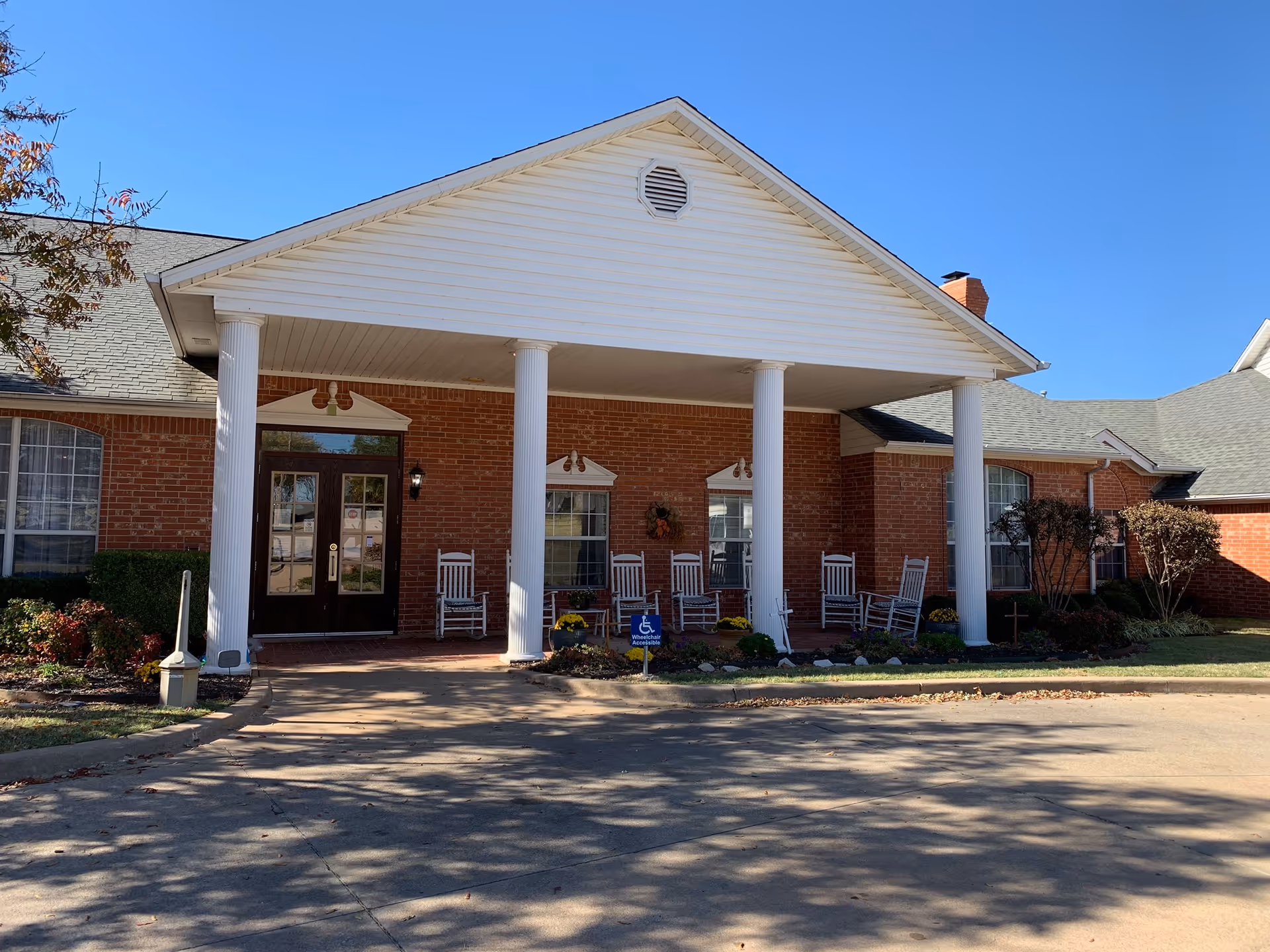 Brick assisted-living facility entrance with white columns, rocking chairs, and a covered front porch.