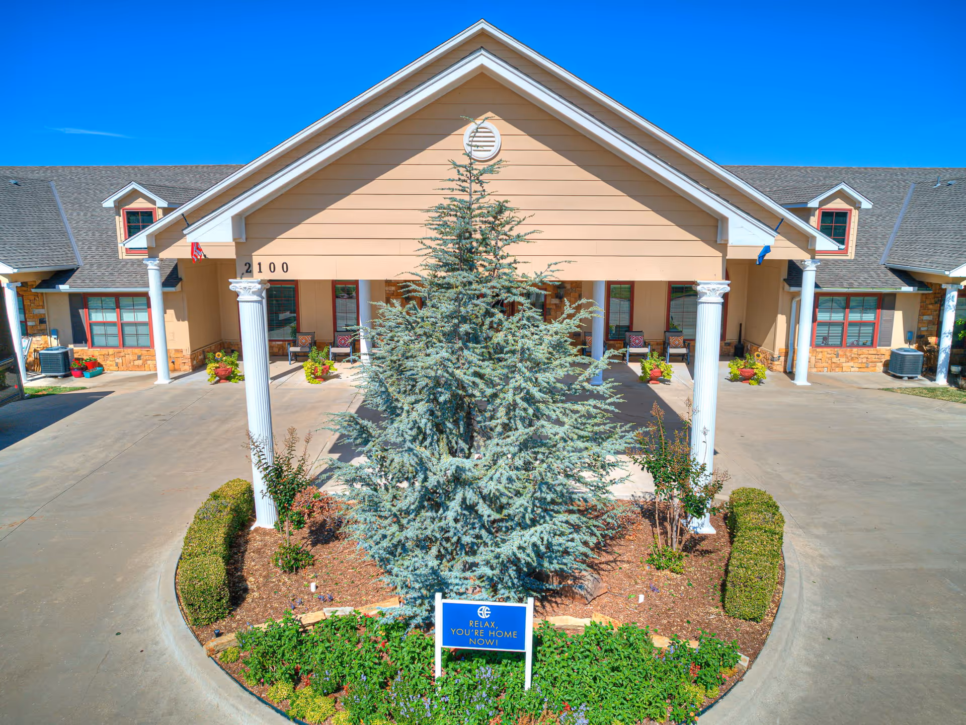 Front view of Silver Elm Estates Norman with a central landscaped tree and curved driveway.