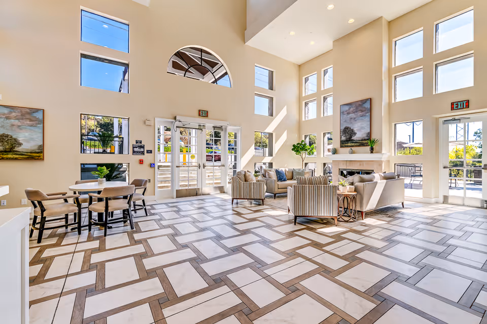 Bright spacious senior living lobby with high ceilings, large windows, patterned tile floor, seating area and fireplace.