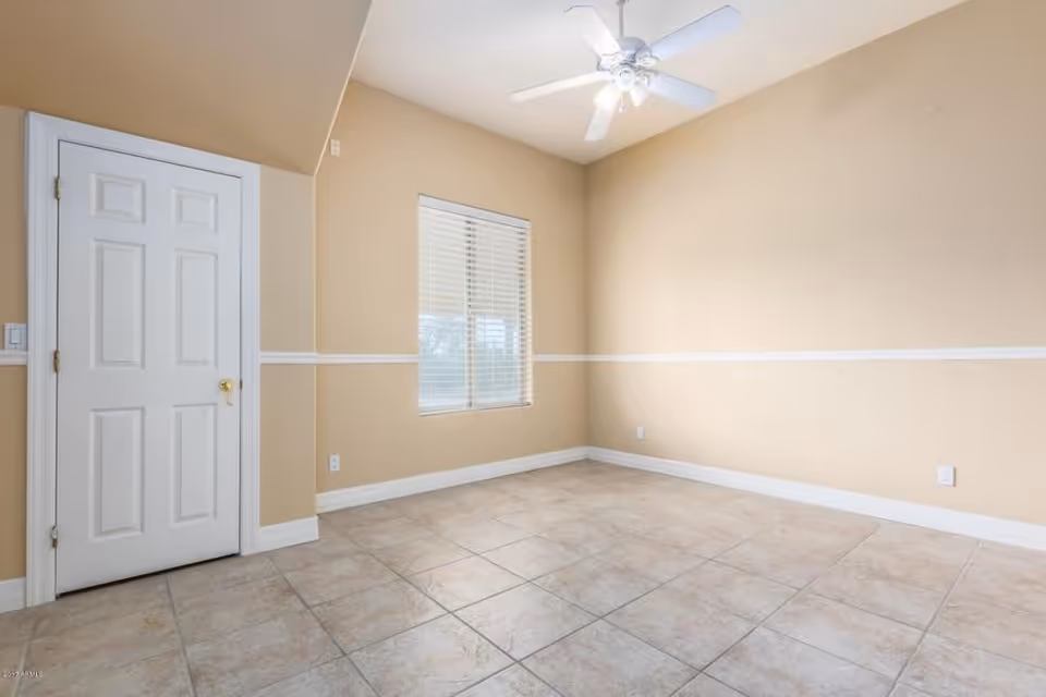 Empty room with beige walls, a white door, a window with blinds, a white ceiling fan, and tiled floor.