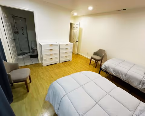Bedroom with two twin beds, a dresser, two chairs, and a visible en-suite bathroom.