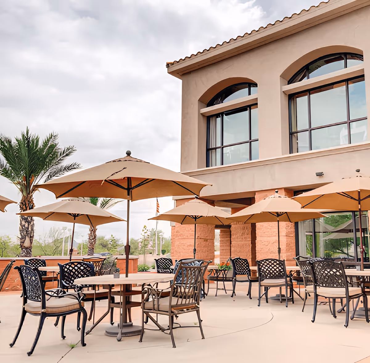 Outdoor patio with tables, chairs, and large umbrellas in front of a stucco building.
