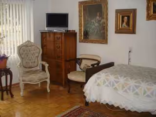 Senior living facility bedroom with bed, dresser, chairs, and framed wall art.