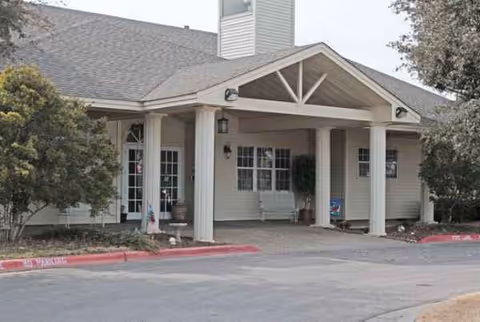 Front entrance of a senior living facility with a covered porch, pillars, and benches.