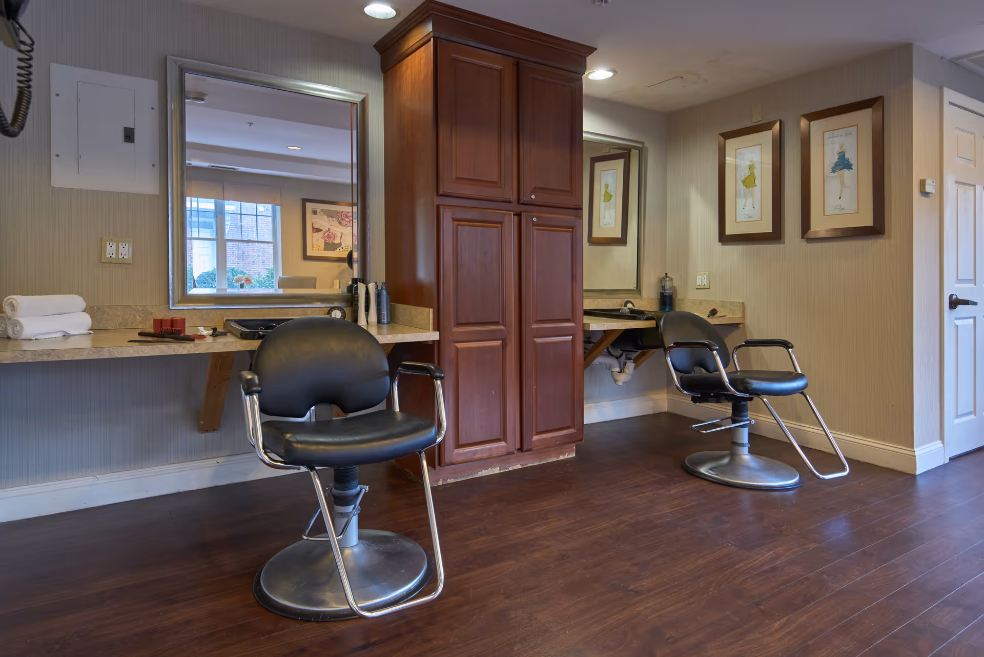Interior salon area with two styling chairs, mirrors, countertops and a central wooden cabinet.