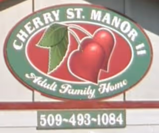Oval sign on a building reading 'Cherry St. Manor II Adult Family Home' with a cherries logo and a phone number.