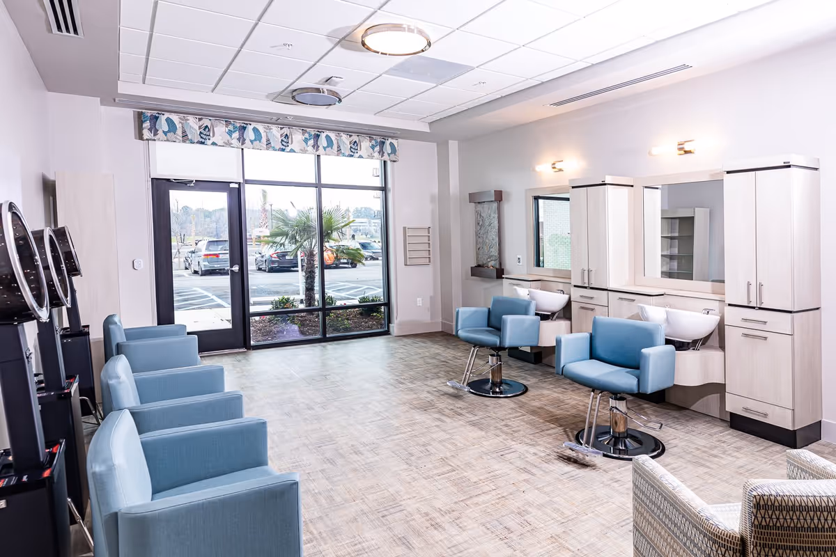 Bright and modern salon area with light blue salon chairs, hair washing stations, large mirrors, and a windowed door showing a parking lot and palm tree outside.