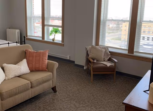 Cozy living area with a beige sofa and armchair next to large windows overlooking the city.