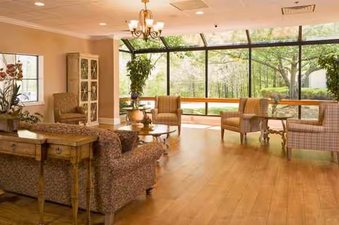 Bright lobby-style living room with sofas, chairs, and large glass windows overlooking greenery.
