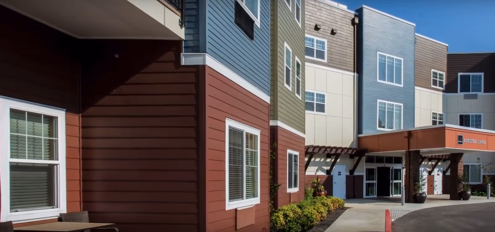 Front entrance of a multi-story assisted living building with colorful siding and a covered drop-off area.