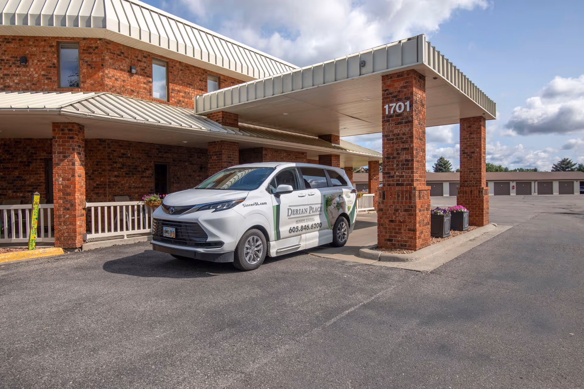 Brick senior living building entrance with a covered porte-cochere and a white Derian Place van parked at the curb.