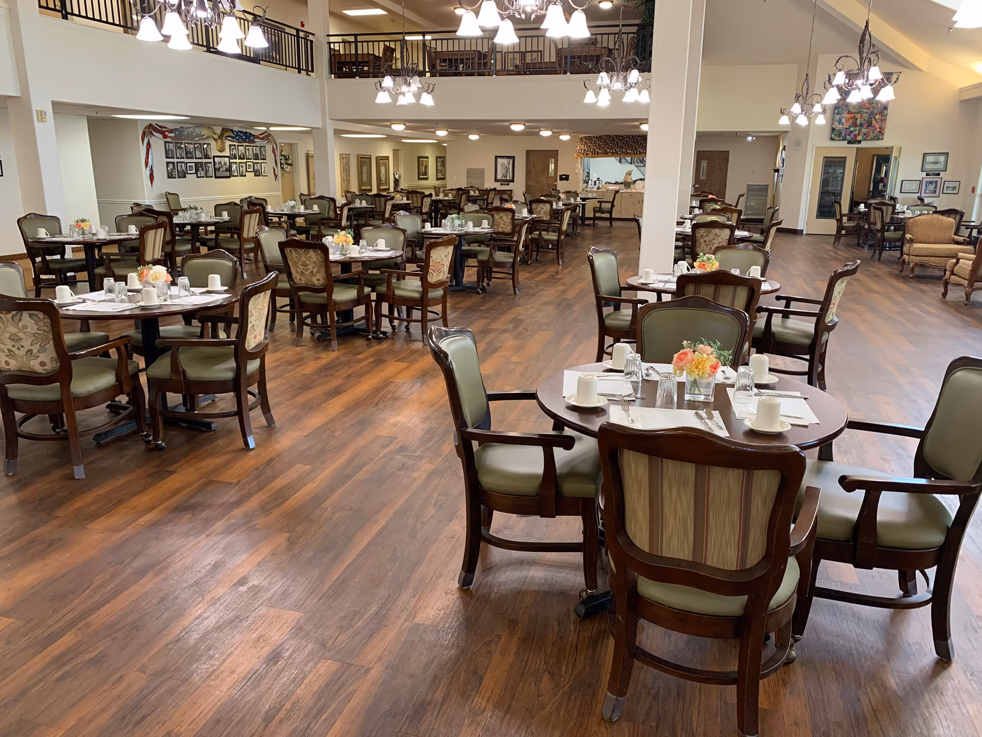 Spacious dining room with many round tables and chairs set with place settings and small floral centerpieces.