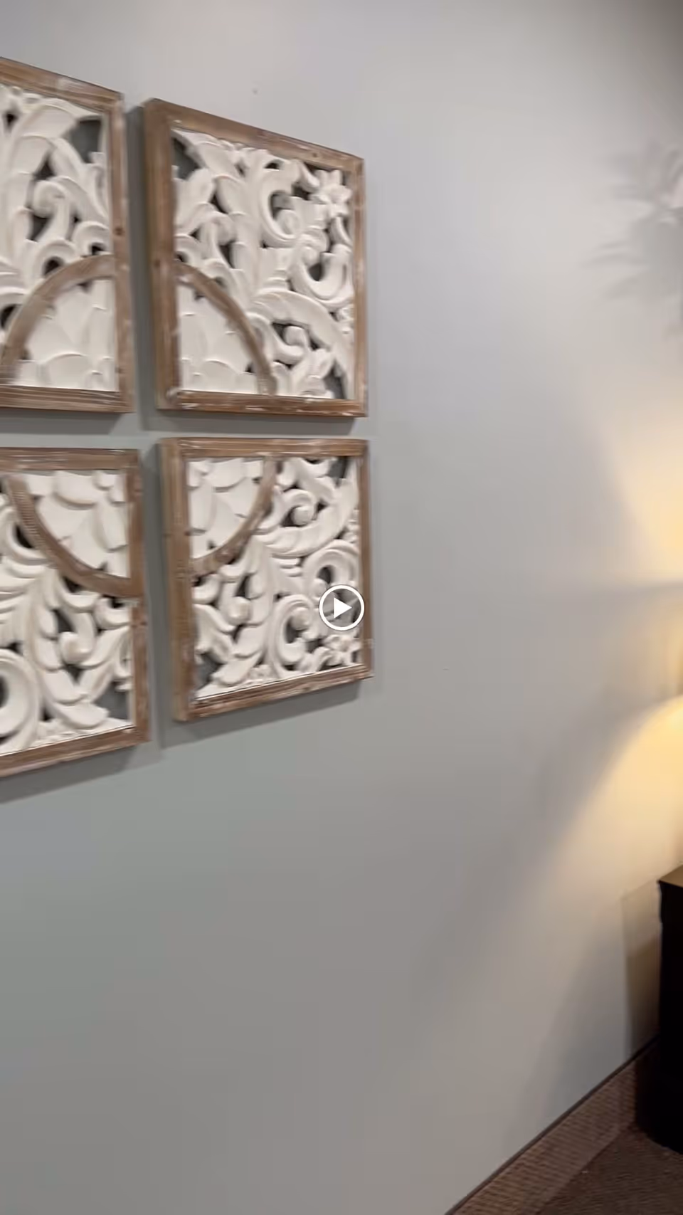 Four decorative carved wooden wall panels on a light-colored interior wall with a lamp and side table visible at the right.