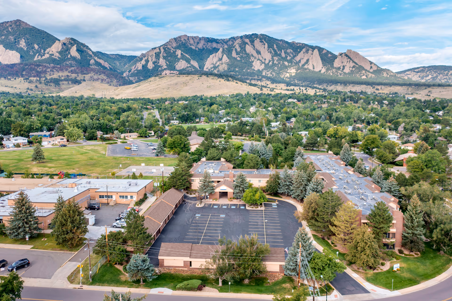 Aerial view of Brookdale Meridian Boulder facility surrounded by trees and residential areas, with a mountainous landscape in the background under a partly cloudy sky.