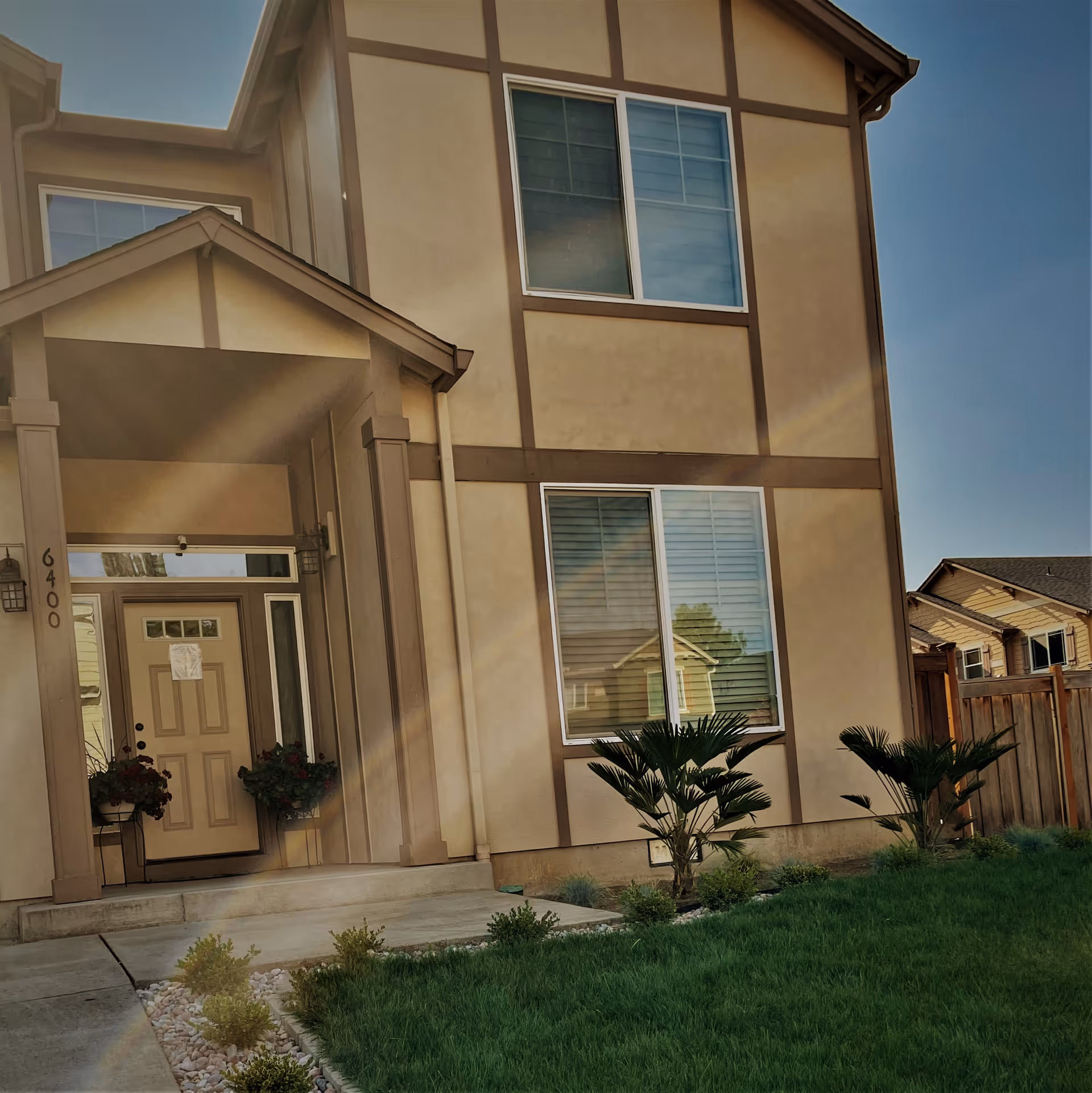 Front exterior of a two-story beige house with a covered entryway, front door, windows, and a small lawn.