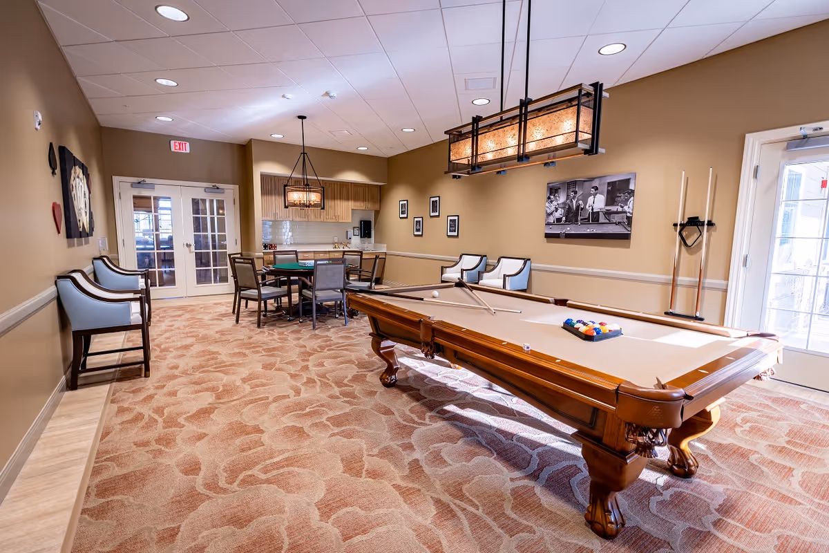 Communal recreation room featuring a pool table, seating, and a dining/game table under warm lighting.
