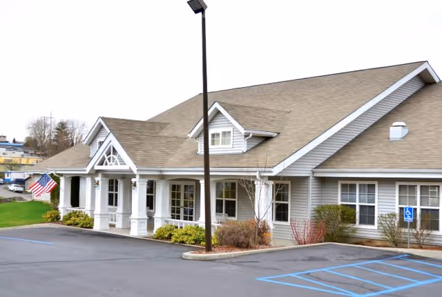 Exterior of Palouse Hills senior living building with a covered porch, white columns, parking lot and an American flag.