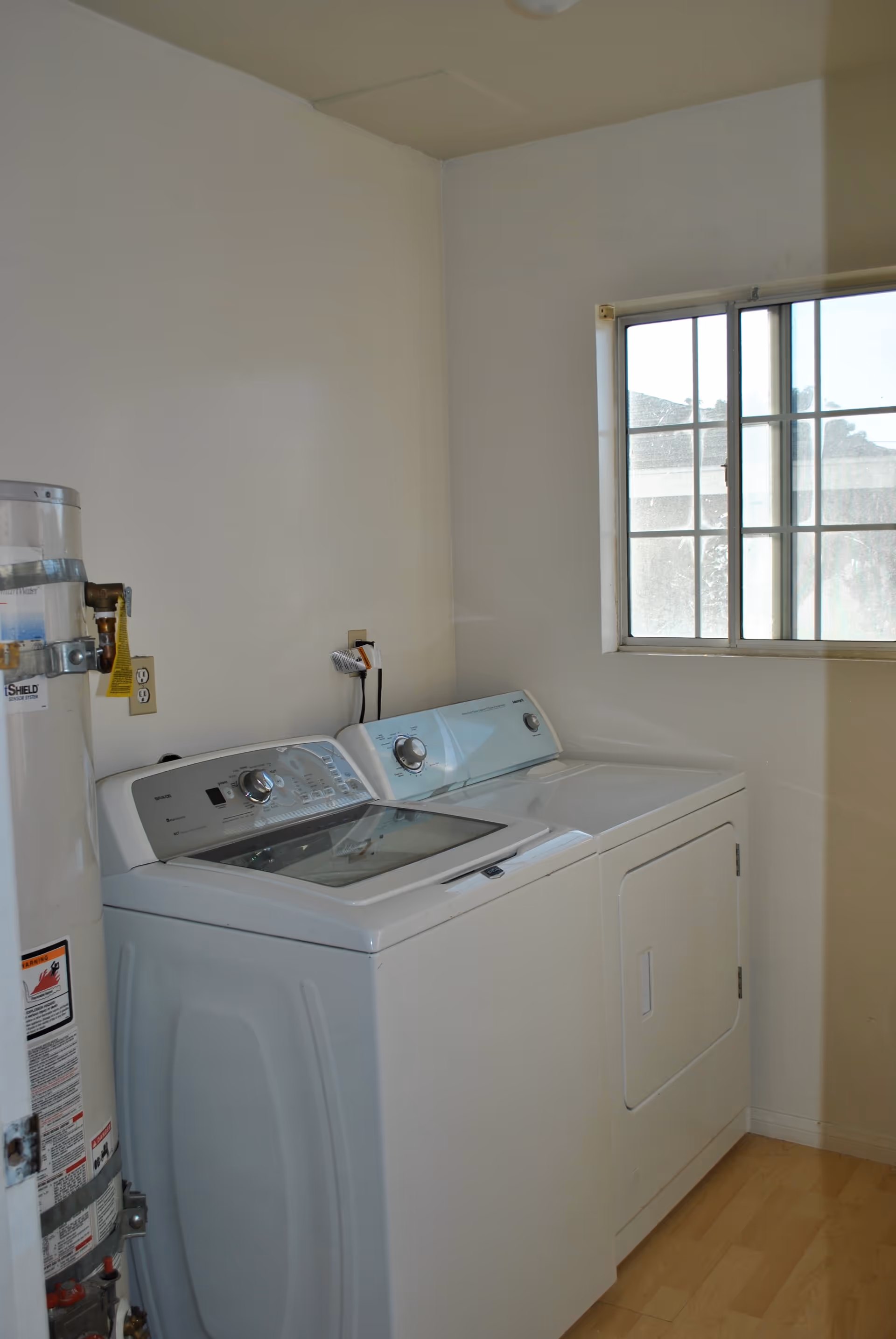 Laundry room with a white washing machine and dryer side by side, a water heater on the left, and a window on the right letting in natural light.