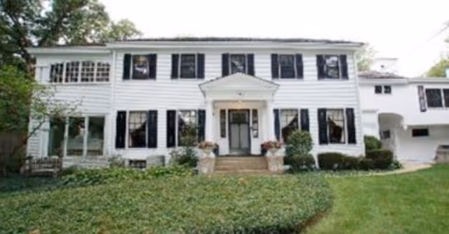 Front exterior of a two-story white colonial-style house with black shutters, a central portico, and a grassy lawn.