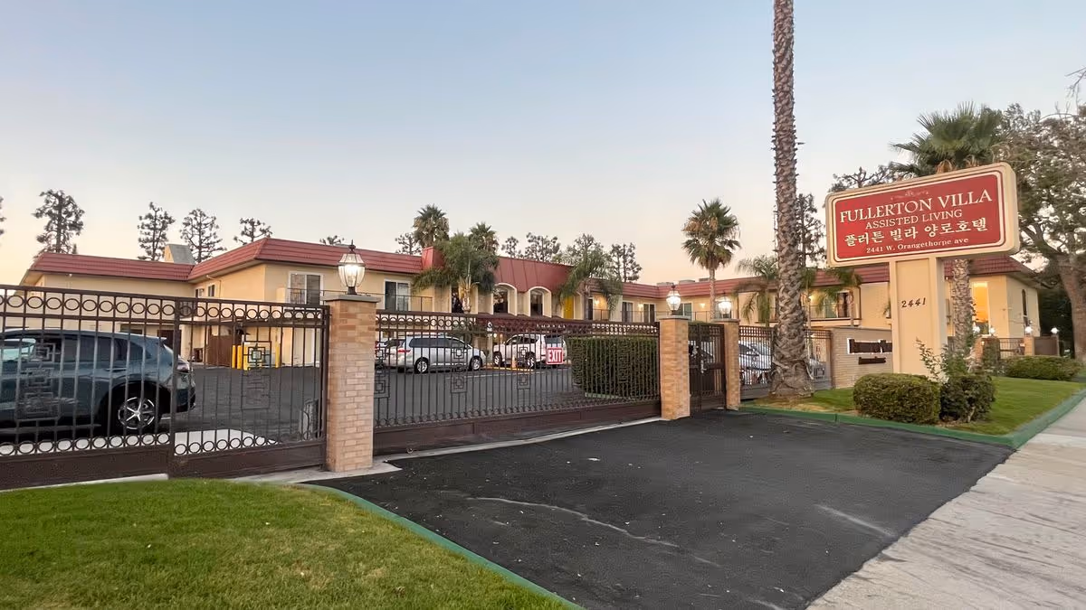 Gated front view of Fullerton Villa assisted living facility with its entrance sign and parking lot.