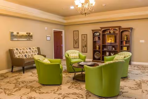 A bright senior living lounge with lime green chairs around a coffee table.
