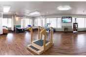 Spacious indoor activity room with exercise equipment, a pool table, and large windows.