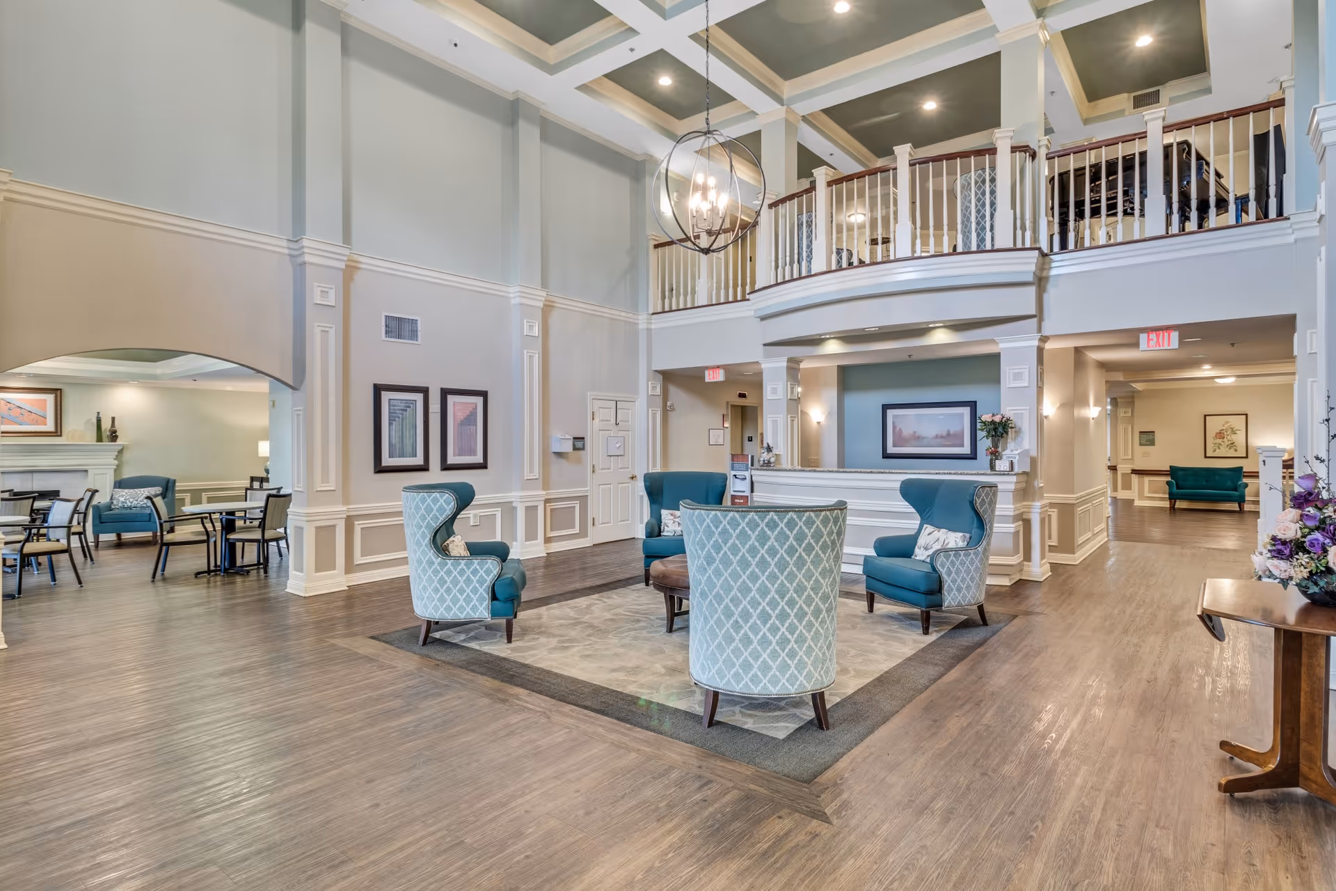 Large two-story lobby in an assisted living facility with a central seating area, reception desk, and second-floor balcony.