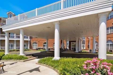 Entrance area of Summit Point facility featuring a covered driveway supported by white columns, surrounded by landscaped greenery and pink flowers, with a brick building in the background.