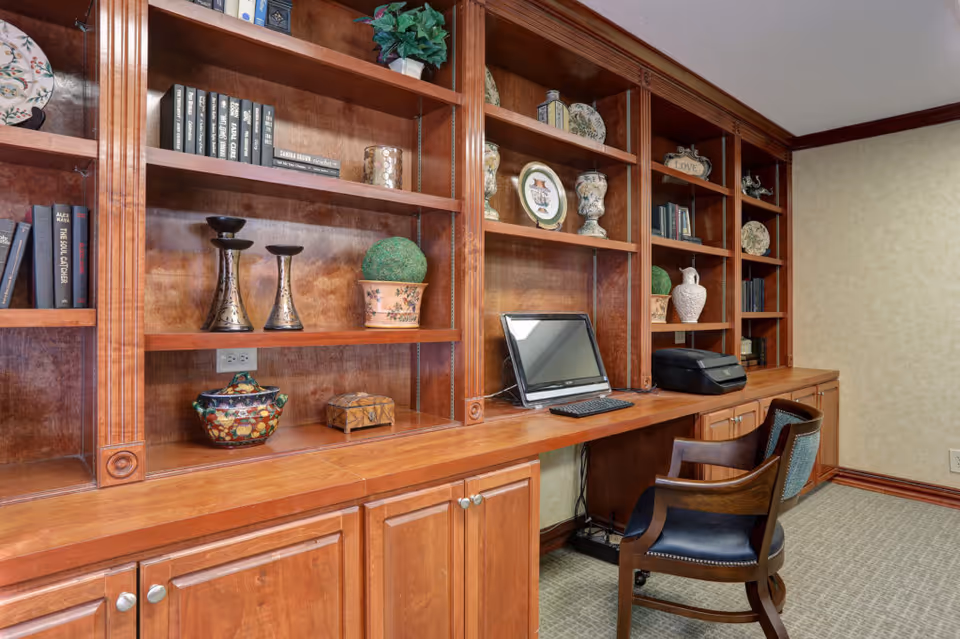 Wood-paneled built-in bookshelves and a desk with a computer and chair in an interior room.
