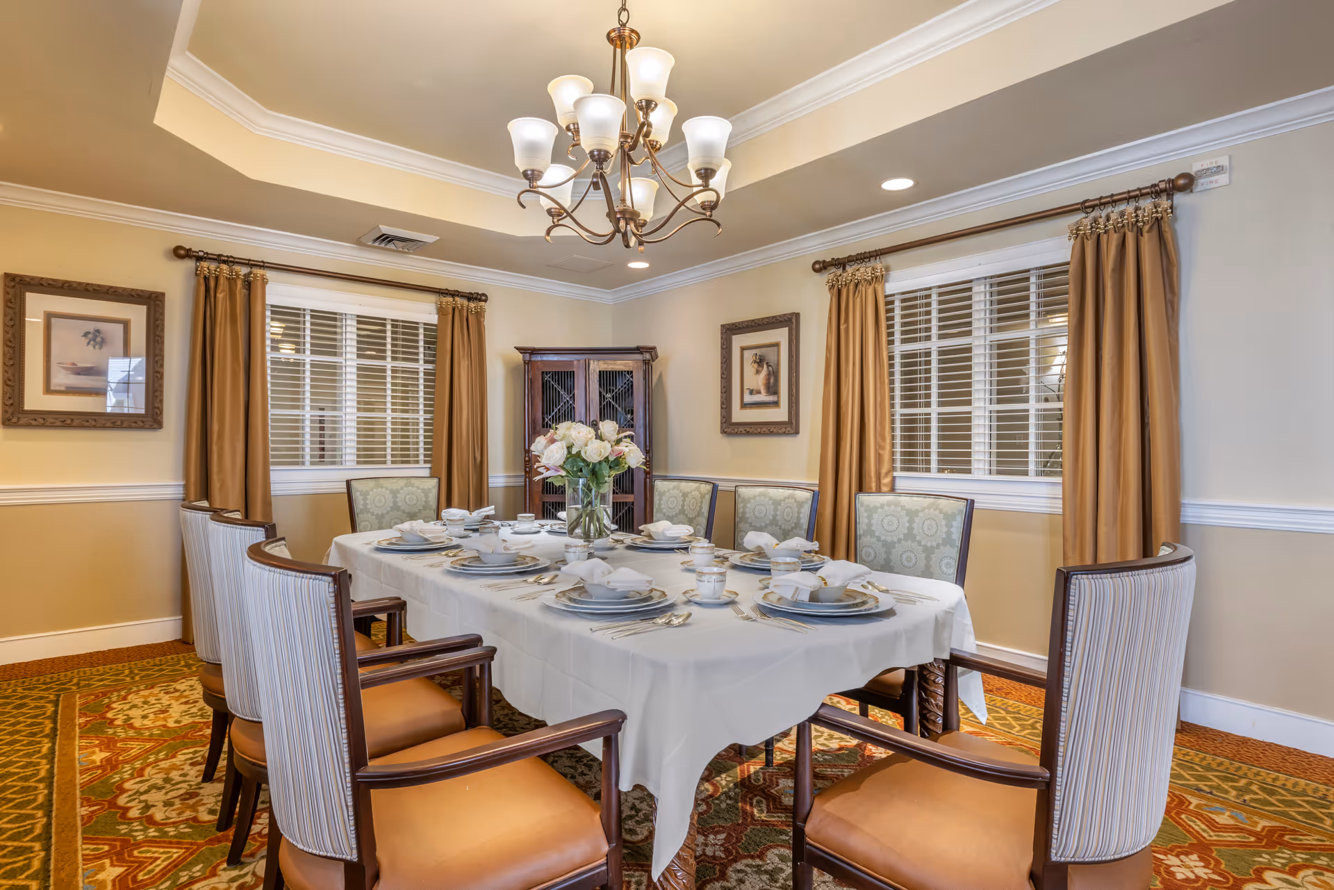 Elegantly set dining table with chairs, a floral centerpiece and chandelier in a formal dining room.
