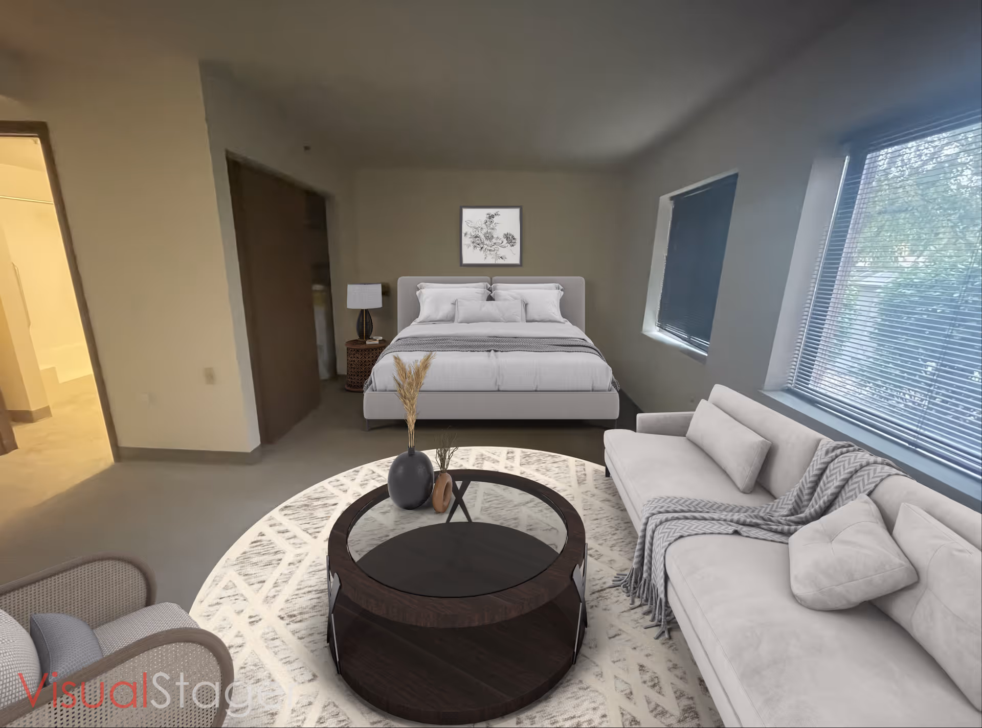 Staged interior showing a living area with a sofa, round coffee table on a rug and a bed against the far wall beneath a framed picture.