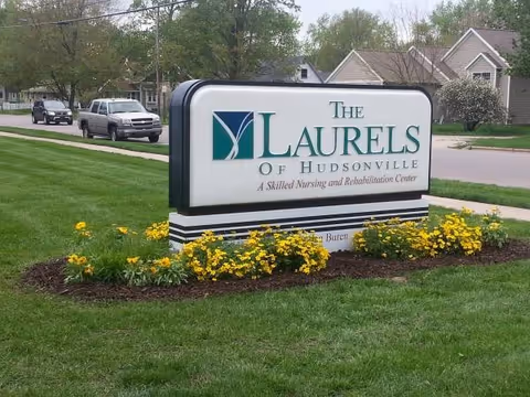 Exterior view of The Laurels of Hudsonville sign on a landscaped lawn with yellow flowers.