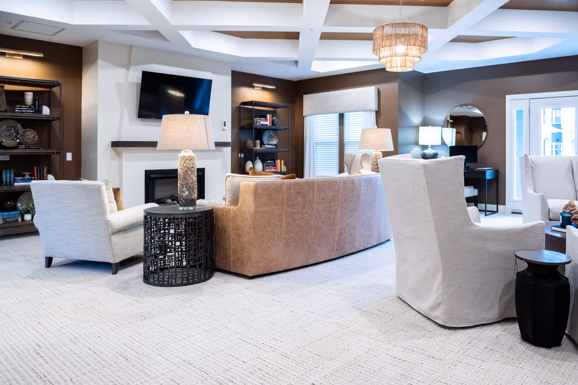 Bright, spacious living room with sofas and armchairs arranged around a fireplace and TV, accented by lamps, bookshelves, and a woven ceiling light.