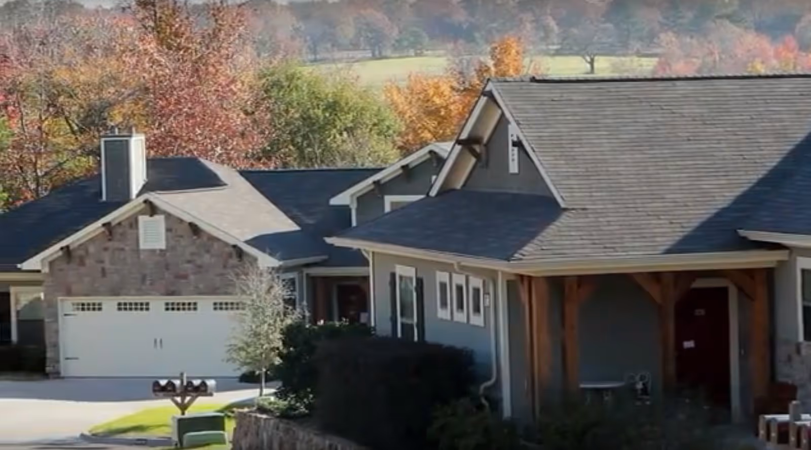 Exterior view of a residential building with a garage, surrounded by trees with autumn foliage in the background.