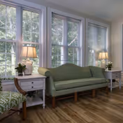 Light-filled sitting area with a green sofa flanked by white side tables and lamps in front of large windows.