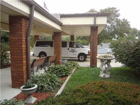 Front entrance of Fayette Caring Center with brick columns, benches, landscaping, and a parked van.