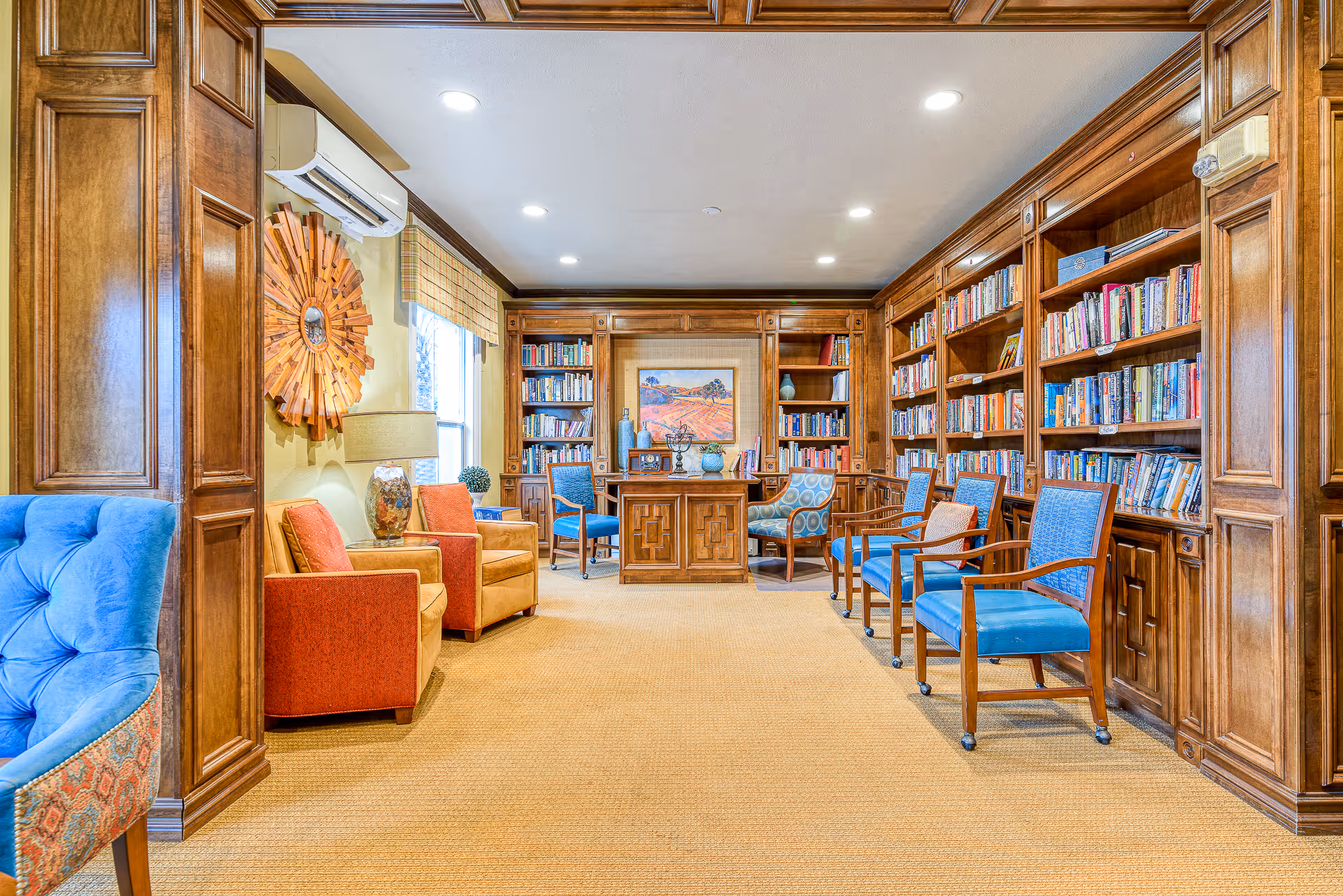 Cozy wood-paneled library lounge with bookshelves, a central desk, and several upholstered chairs.
