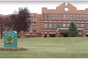 Brick healthcare building with a manicured lawn, trees, and a foreground sign.