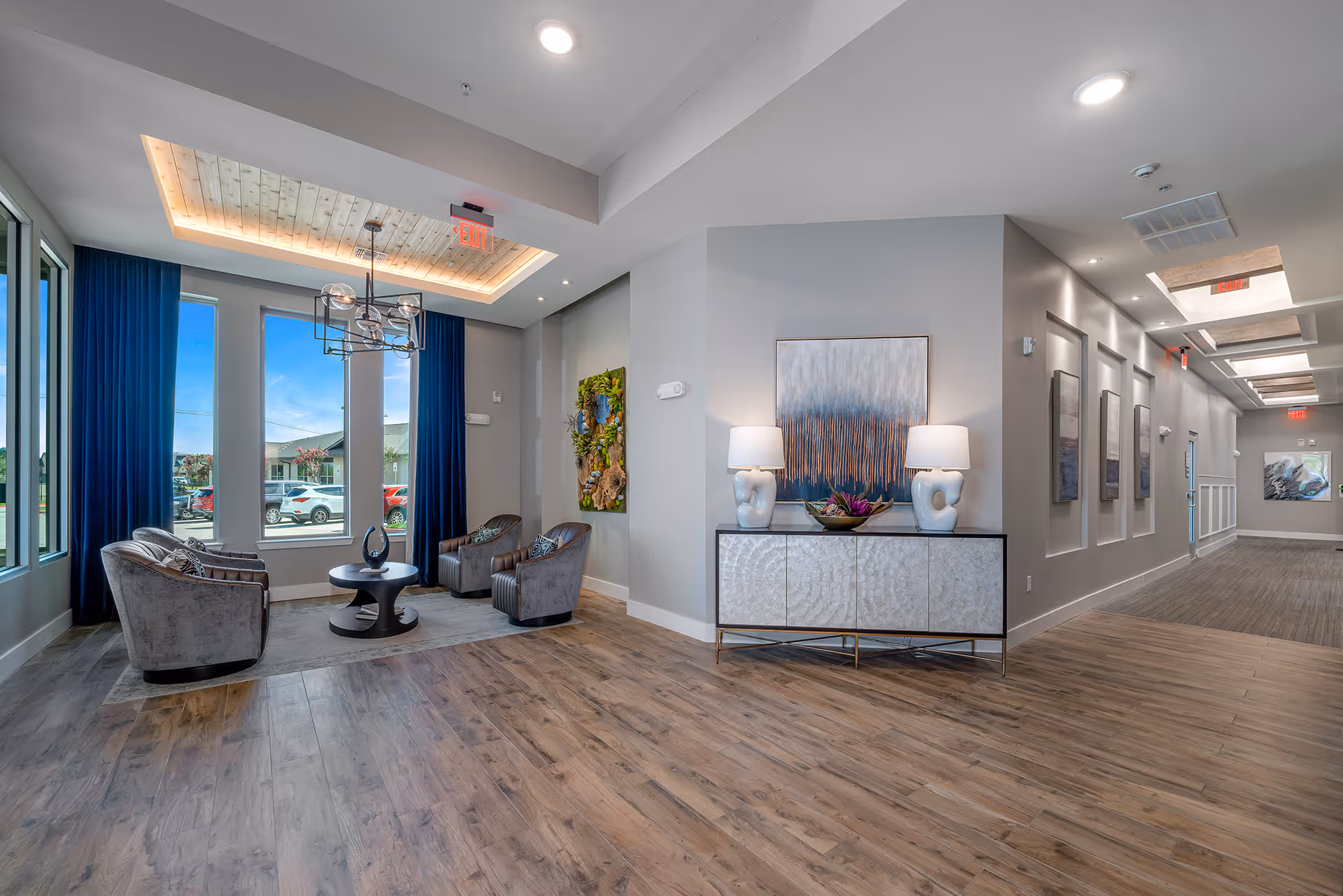 Modern senior living lobby with a seating area, console table with lamps and artwork, and large windows letting in daylight.