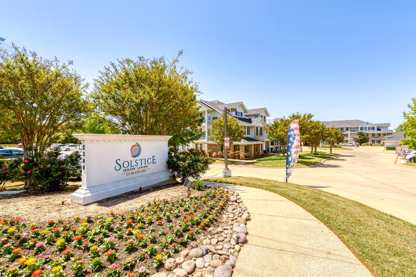 Entrance sign for Solstice Senior Living amid landscaped flowerbeds with multi-story senior living buildings and a driveway in the background.