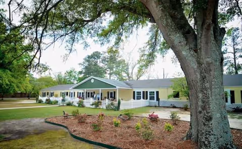 Single-story building with green roof, yellow walls, front porch, and landscaped garden.