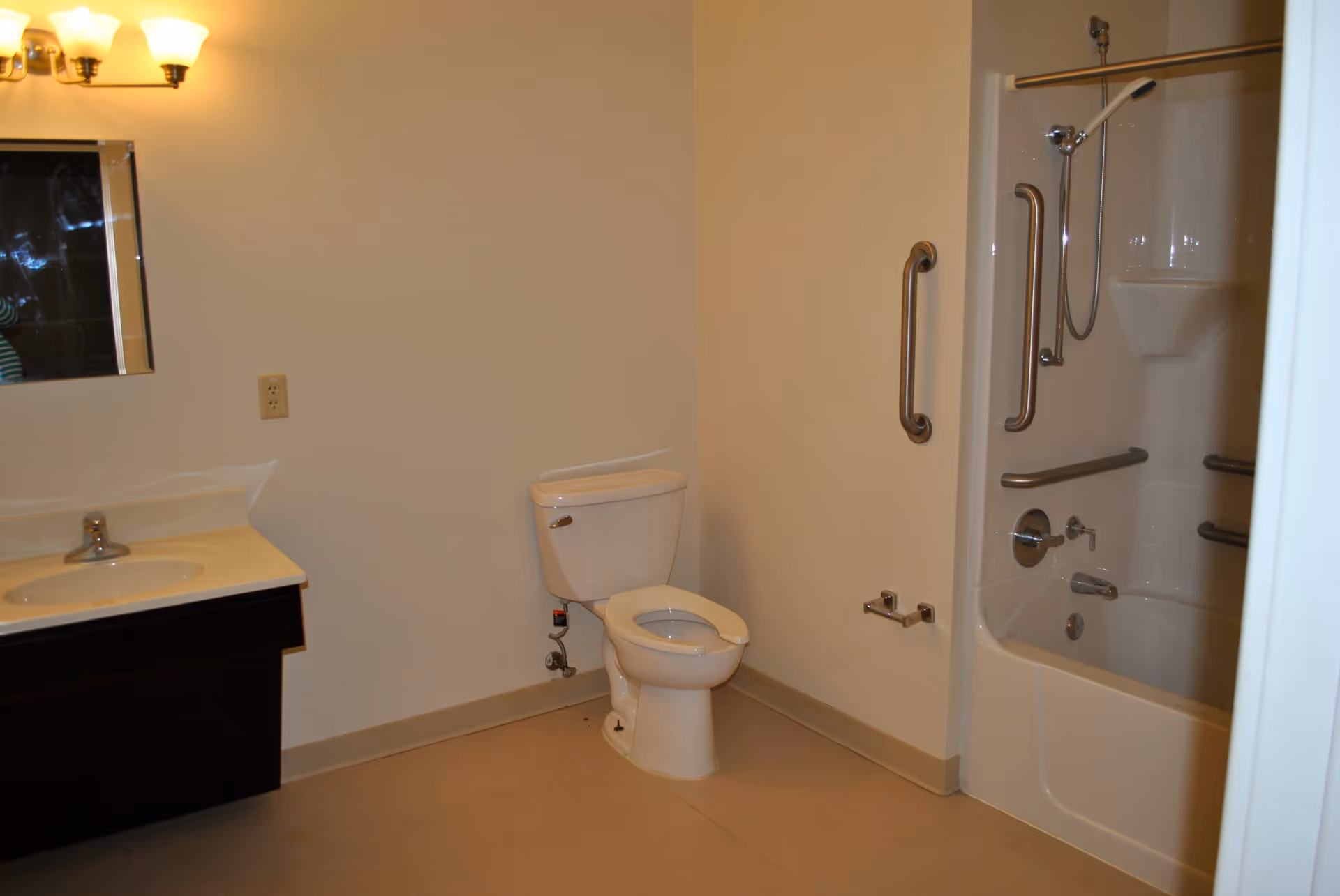 Accessible bathroom with a toilet, sink vanity, and a shower/tub equipped with grab bars.