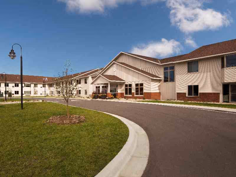 Front exterior of a two-story senior living building with a curved driveway, lawn, and entrance.