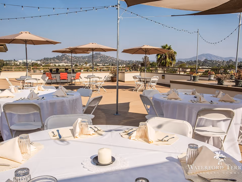 Rooftop patio set up for outdoor dining with round tables dressed in white linens, umbrellas, and distant hills in the background.