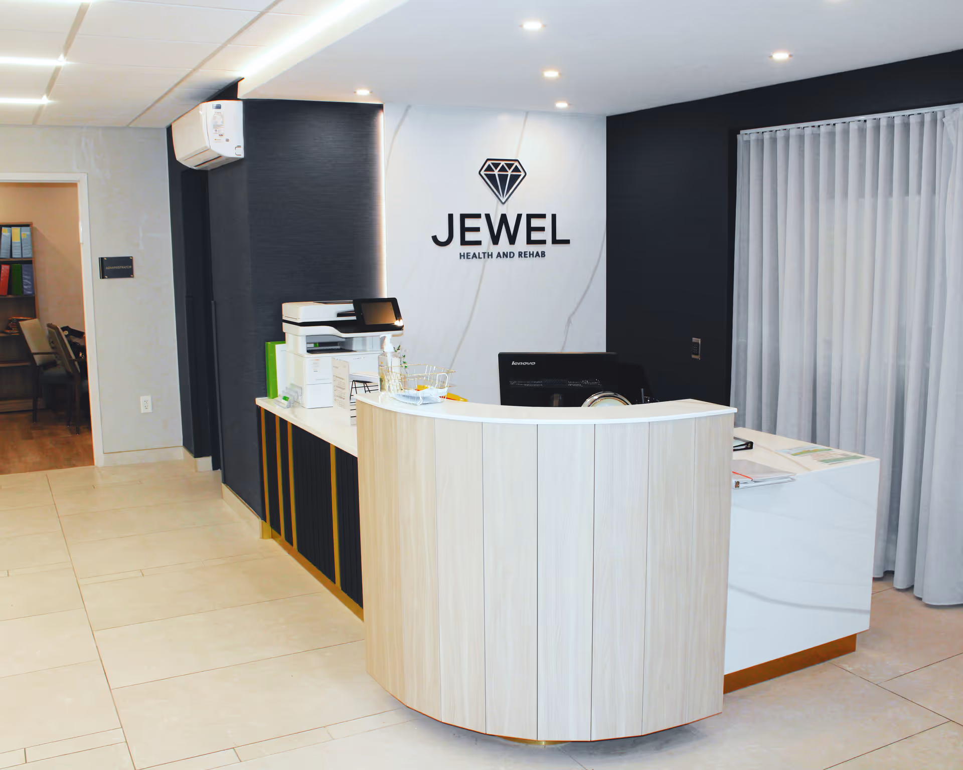 Reception area with a curved wooden front desk and the 'JEWEL Health and Rehab' logo on the wall behind it.